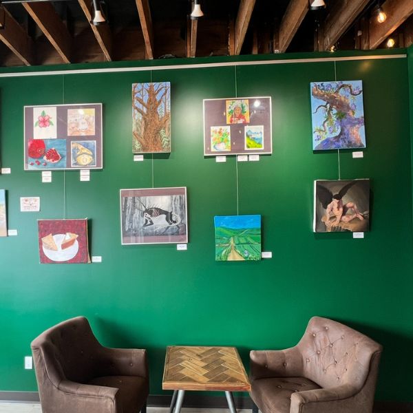 Group of five adults engaged in an art or crafting activity around a long table in a brightly lit community room