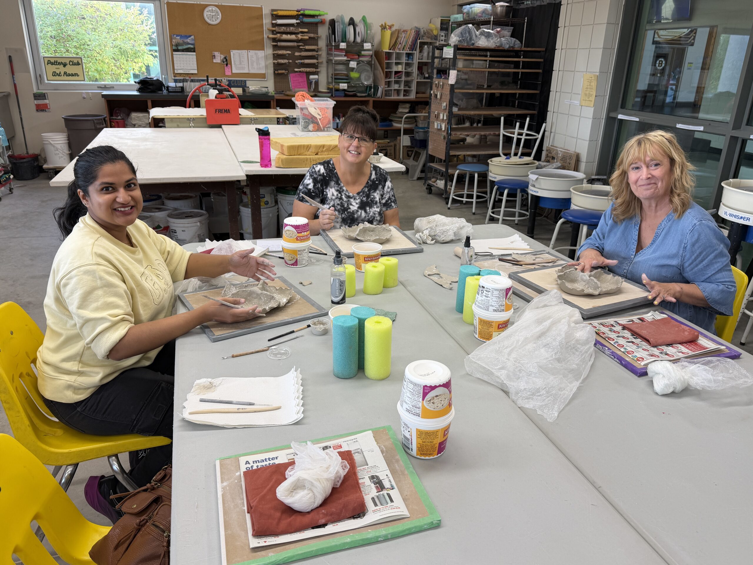 Group of ten smiling women posing in a classroom and holding up small, colorful woven textile swatches